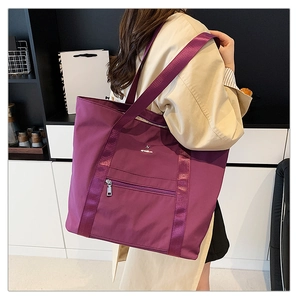 Gros plan d'un sac cabas en nylon bordeaux avec poche zippée et logo métallique