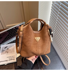 Gros plan sur un sac seau en daim marron avec logo triangle doré et charm en perles de bois