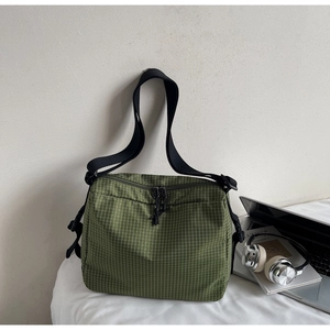 Detail of green plaid canvas crossbody bag with adjustable strap and dual zippers