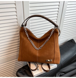 Detail of brown faux suede tote bag featuring silver chain and leather handle with white stitching