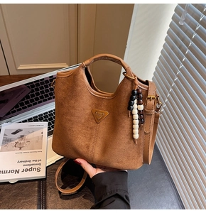 Gros plan du sac seau en cuir marron mat avec logo triangle et pendentif à perles