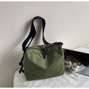 Detail of green checkered canvas crossbody bag with adjustable strap and zip closure