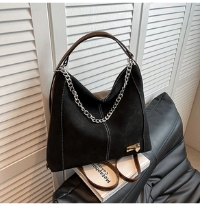 Close-up of black matte suede tote bag with brown leather strap and silver chain detail