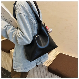 Detail of black leather bucket bag with a cute koala plush charm worn by model