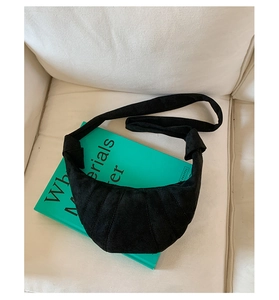 Détail d'un sac croissant noir en daim mat posé sur un livre vert sur un canapé blanc