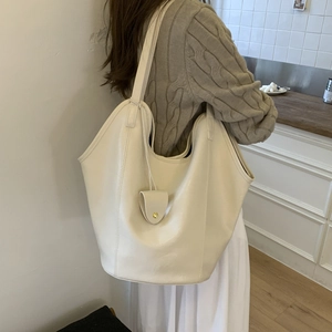 Detail of cream white large tote bag with matching charm on a cozy knit sweater