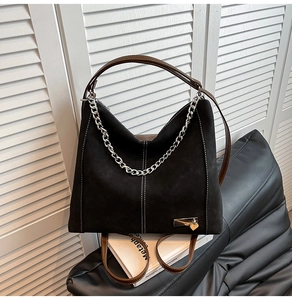 Detail of black suede tote bag with white stitching and silver heart pendant
