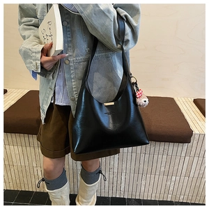 Detail of black faux leather bucket bag featuring gold metal accents and plush charm pendant