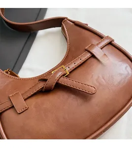 Detailed close-up of brown textured leather crescent bag with golden metal buckle detail