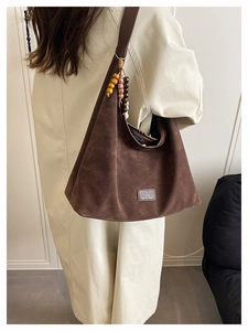 Détail d'un sac porté épaule vintage en daim marron avec pompon et logo en cuir