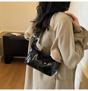 Detail of glossy black patent leather shoulder bag with silver hardware on trench coat