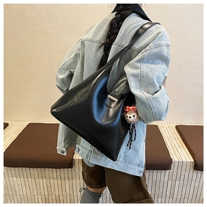 Detail of black PU leather tote bag with silver trim and plush charm worn by model