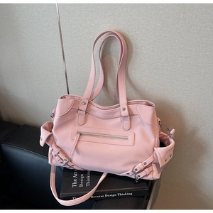 Detail of pink faux leather tote bag with metal zipper and side buckle straps on a sofa