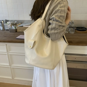 Side view of minimalist cream leather tote bag with small gold snap button charm