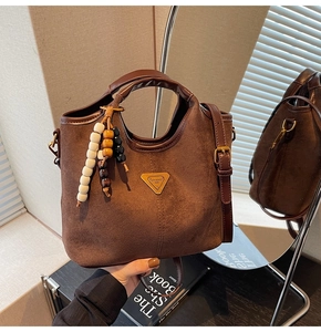 Détail du sac seau en daim marron foncé avec logo doré et pendentif perlé