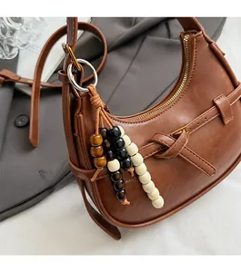 Detail of a brown leather crescent handbag with wooden beaded charm and metal zipper