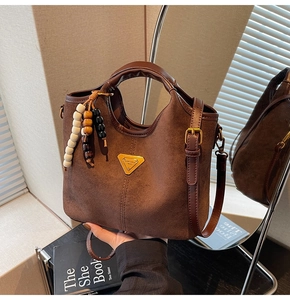 Détail du sac seau en daim marron foncé avec logo métallique doré et charm perlé