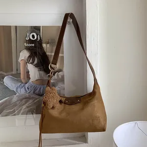 Close-up of brown suede tote bag featuring leather logo patch and cute teddy bear charm