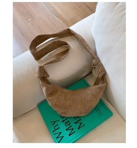 Sac croissant en daim marron avec nœuds exposé sur un livre et un canapé blanc