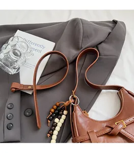 Detail of brown vintage crescent bag showing decorative woven straps and beaded pendant