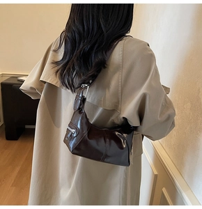 Detail of dark brown glossy hobo bag with adjustable silver buckle worn by model