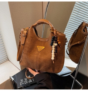 Gros plan sur le sac seau marron mat avec logo doré et breloque décorative en bois
