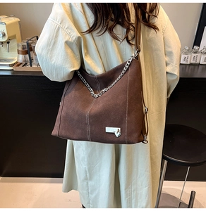 Detail of dark brown suede shoulder bag with silver chain and heart charm in a cafe setting
