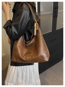 Détail d'un grand sac hobo en cuir marron mat avec breloque en perles vintage et texture douce