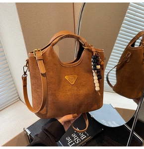 Détail montrant la texture en daim marron et le logo métallique doré sur le sac à main