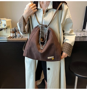 Detail of dark brown hobo tote bag featuring a silver chain and heart pendant in a cafe