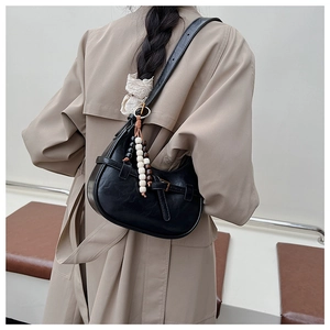 Detail of a vintage black crescent bag with bead charm worn over a khaki trench coat
