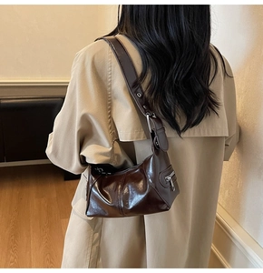 Shoulder view of a dark brown glossy patent leather bag with silver metal details