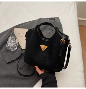 Détail d'un sac seau noir mat avec logo triangulaire doré et bandoulière réglable