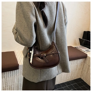 Close-up of a vintage brown leather dumpling bag with buckle detail and bead pendant