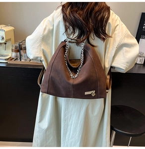 Detail of dark brown suede tote bag with silver chain and heart charm in a cafe setting