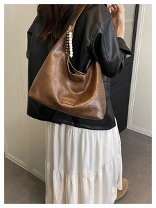 Détail du sac Hobo marron avec texture en cuir mat et breloque décorative en perles