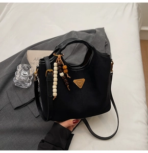 Détail du sac seau noir mat avec logo triangle doré et charms en perles de bois