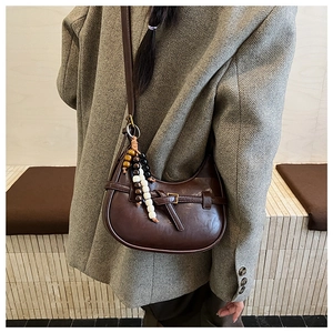 Detail of dark brown crescent bag with decorative strap buckle and beaded pendant accessory