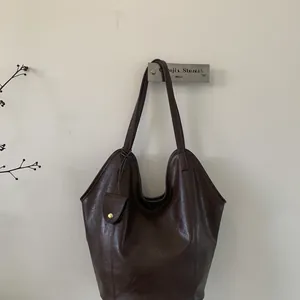 Detail of dark brown leather tote bag featuring a minimalist design and gold button charm
