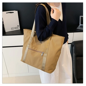 Sac fourre-tout en nylon kaki avec large bandoulière et poche zippée porté par un mannequin