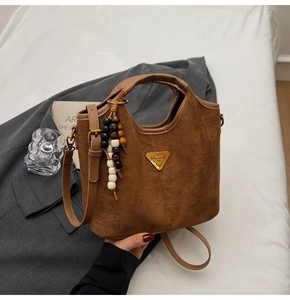 Détail du sac seau marron mat avec logo triangulaire et breloque en perles de bois rétro