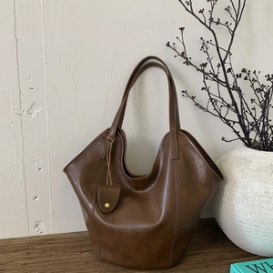 Detailed view of dark brown leather tote bag with unique curved opening and mini charm pouch