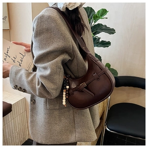 Detail of dark brown leather half-moon bag with decorative beads on a model wearing a suit