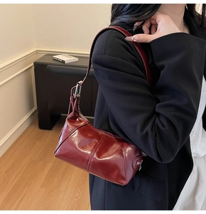 Close-up of a dark red glossy patent leather hobo bag with sleek metallic buckle details