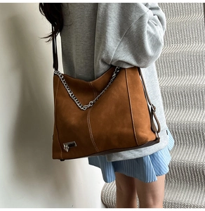 Brown suede tote bag with silver chain and heart charm detail shown on model