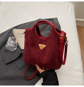 Détail du sac seau bordeaux mat avec plaque logo en métal et finitions en cuir lisse
