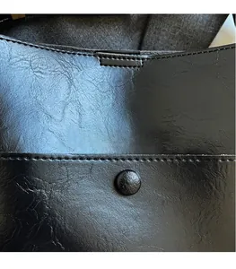 Close-up of black leather bucket bag showing oil-wax texture and precise stitching