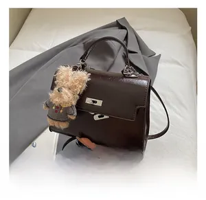 Detail of dark brown patent leather handbag with metal turn-lock and teddy bear charm
