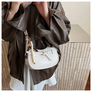 Detail of minimalist cream half-moon crossbody bag with vintage beaded charm on a model
