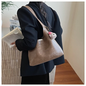 Brown vintage leather shoulder bag with plush owl charm shown on model in black suit